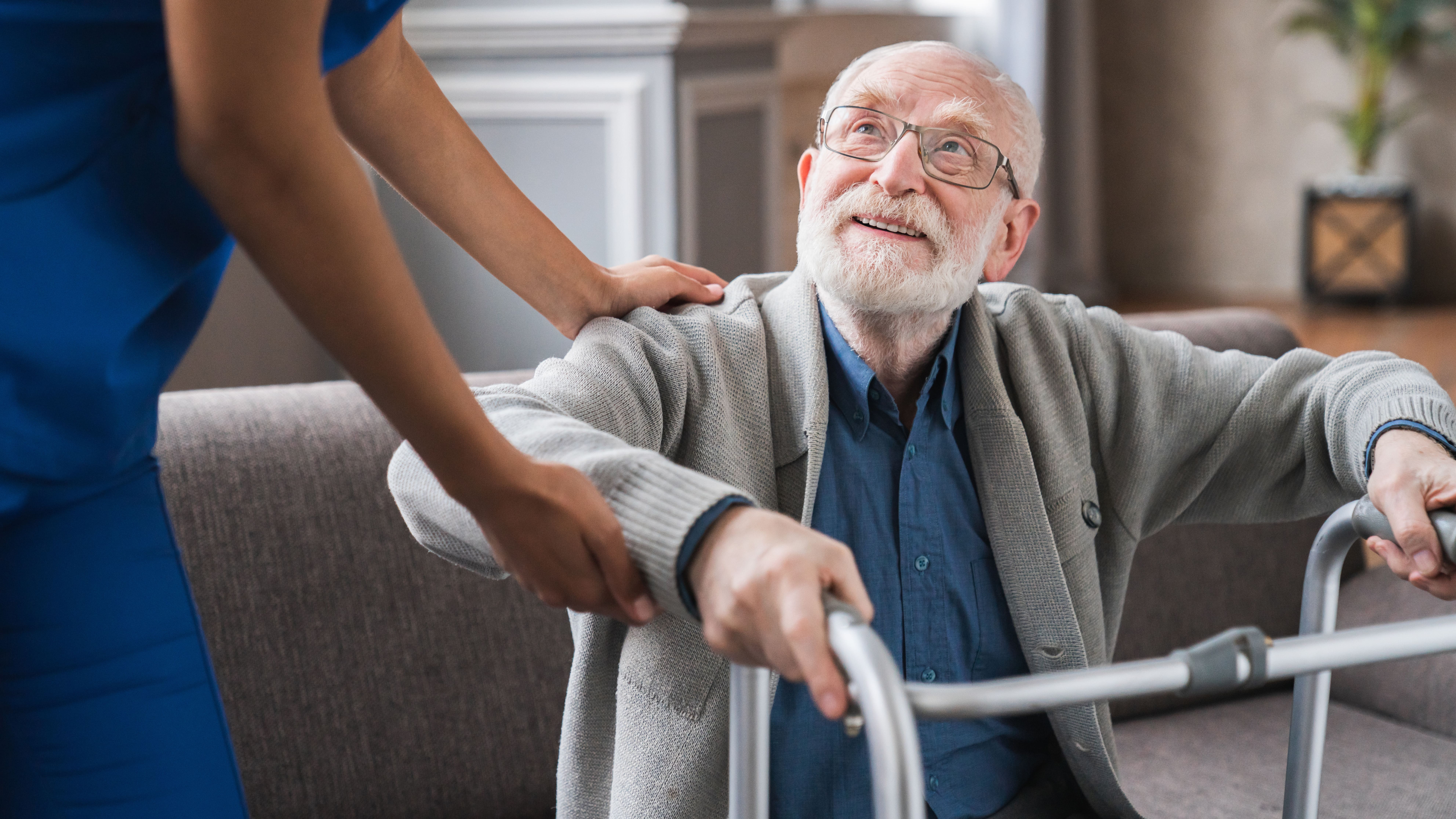 Helping a senior in need stand up, using a walker.